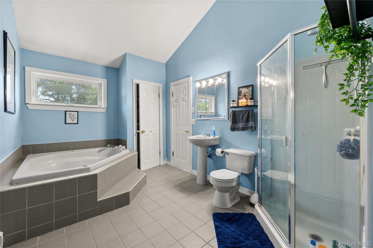 Spacious primary and bathroom featuring a built-in soaking tub with tiled surround, a separate glass-enclosed shower, pedestal sink, and a window prov