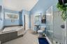 Spacious primary and bathroom featuring a built-in soaking tub with tiled surround, a separate glass-enclosed shower, pedestal sink, and a window prov