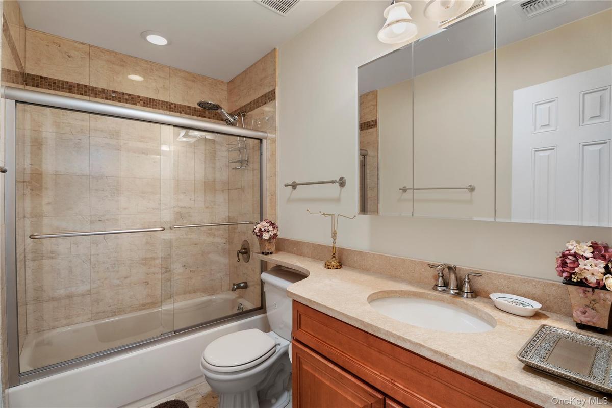 Full bathroom featuring enclosed tub / shower combo, toilet, vanity, and visible vents