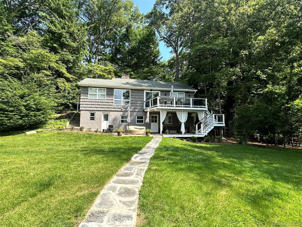 View of front facade featuring stairs, a chimney, a front lawn, a wooden deck, and a patio