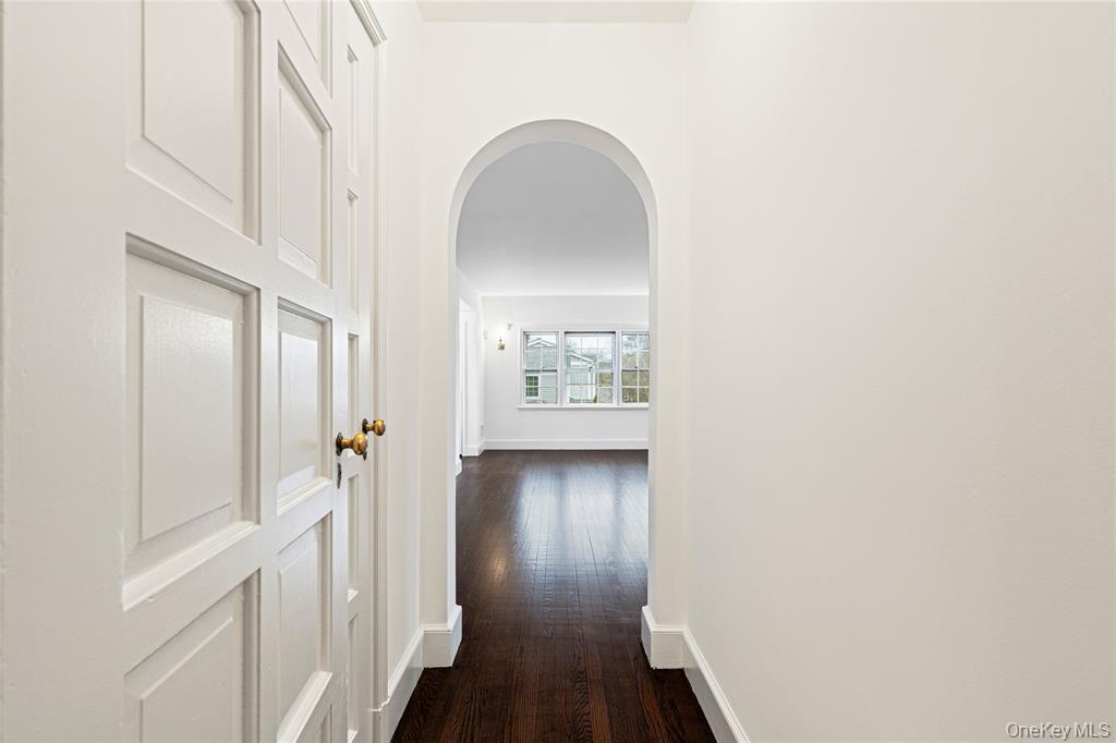 Corridor with arched walkways, dark wood-style flooring, and baseboards