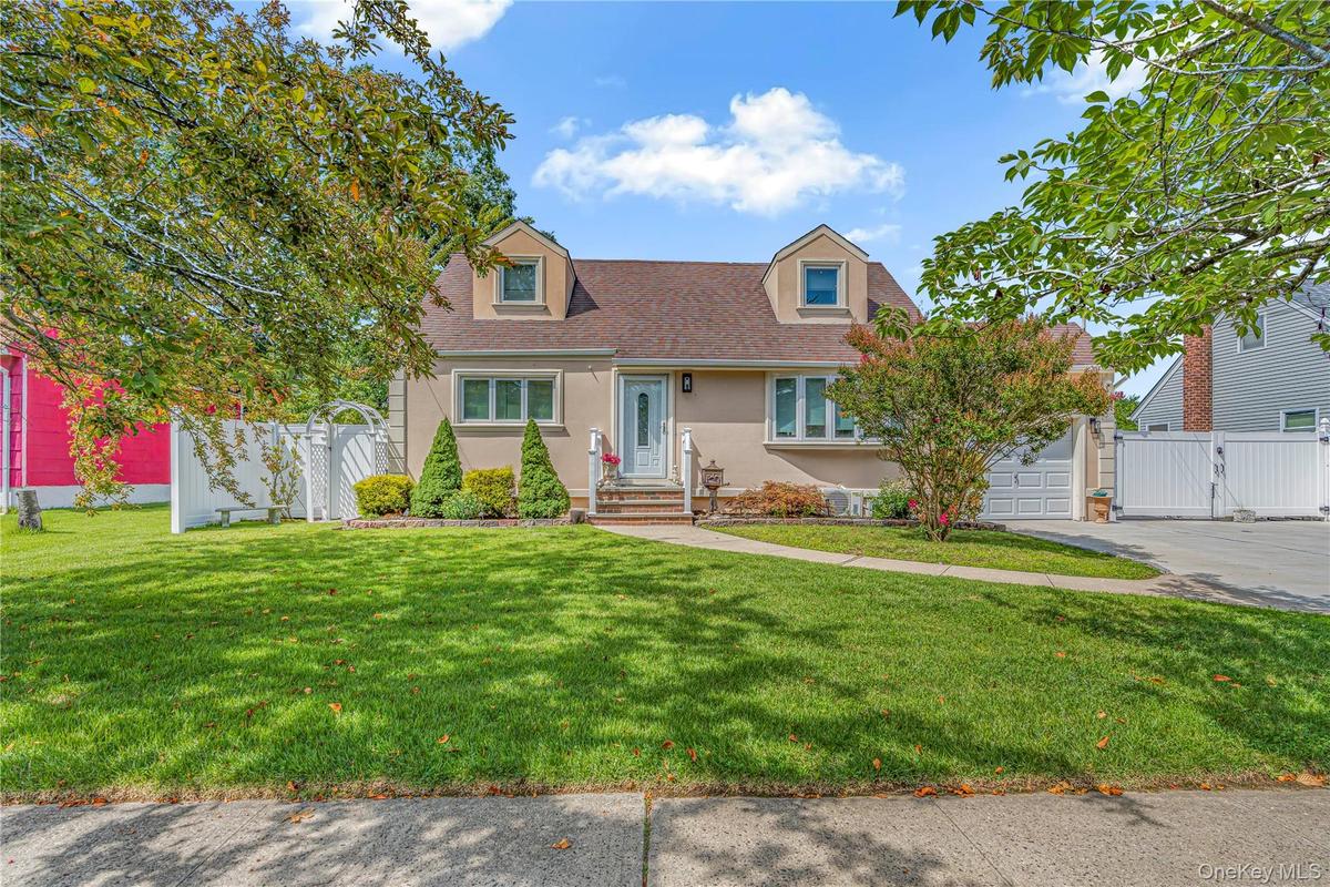 Stucco exterior with dormer windows, a concrete driveway, and a white fence