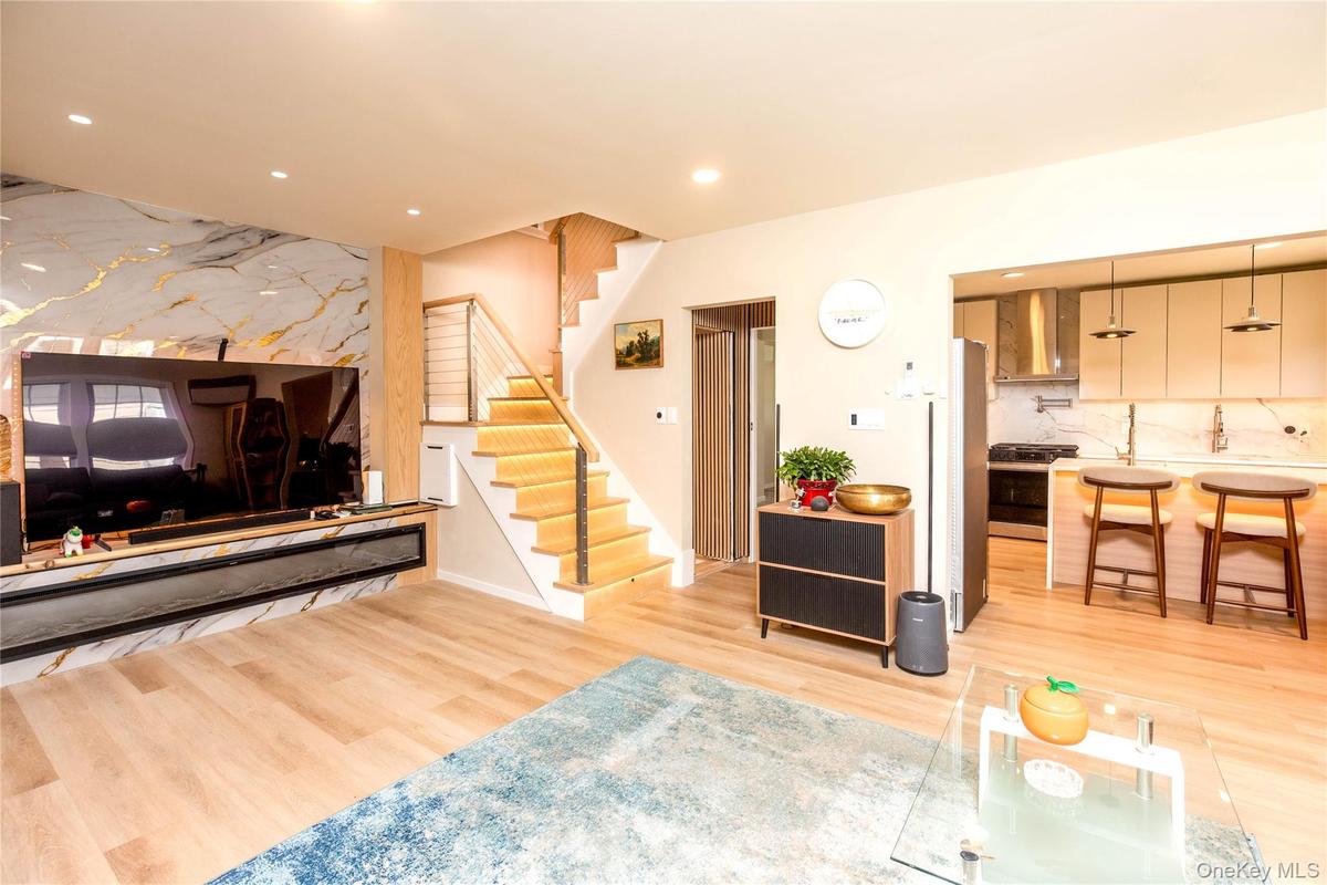 Open-concept living area featuring light wood-finish flooring, recessed lighting, and a modern staircase with cable railing