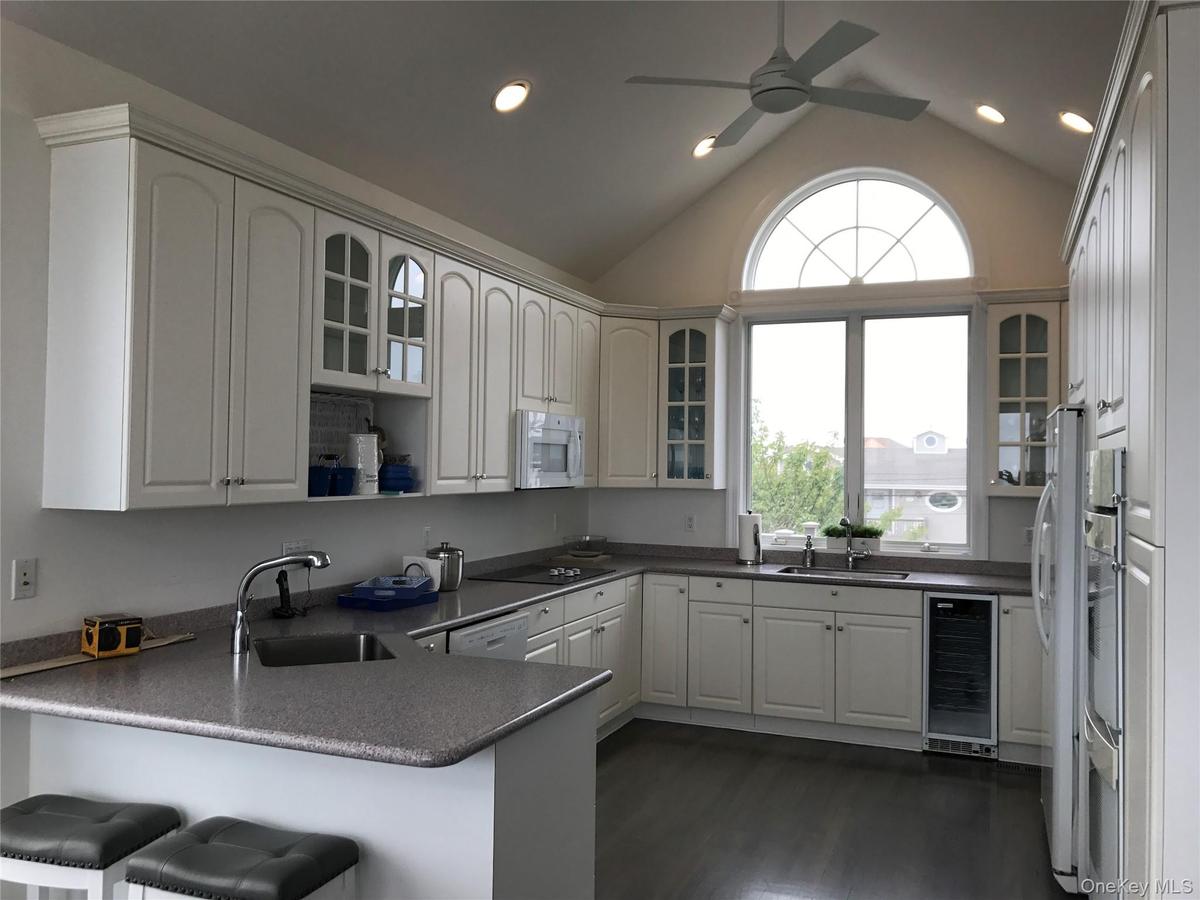 Kitchen featuring glass insert cabinets, a peninsula, vaulted ceiling, white cabinets, and wine cooler