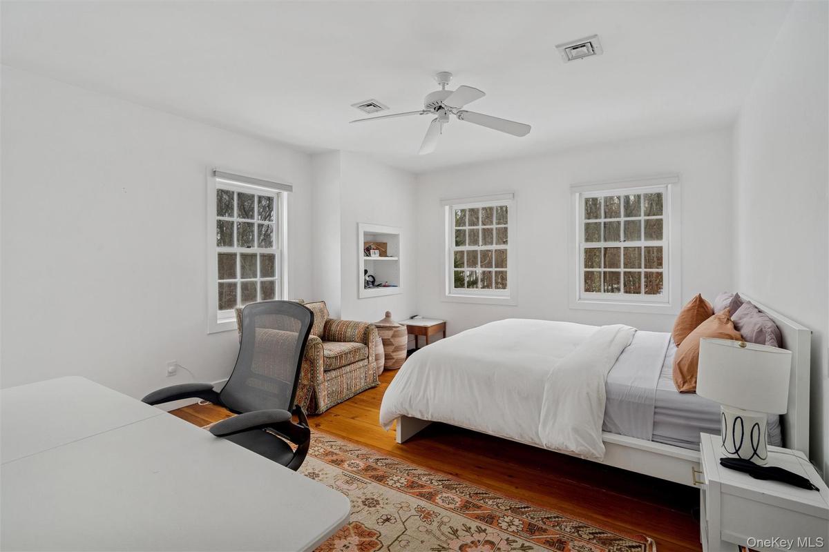Bedroom with wood finished floors, a ceiling fan, an office area, and multiple windows