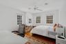 Bedroom with wood finished floors, a ceiling fan, an office area, and multiple windows