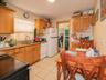 Kitchen featuring white appliances, ornamental molding, light tile patterned flooring, light stone counters, and brown cabinetry