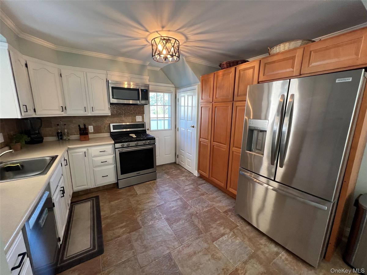 Kitchen featuring tile flooring, stainless steel appliances, white cabinetry with dark hardware, and light wood-finish cabinetry