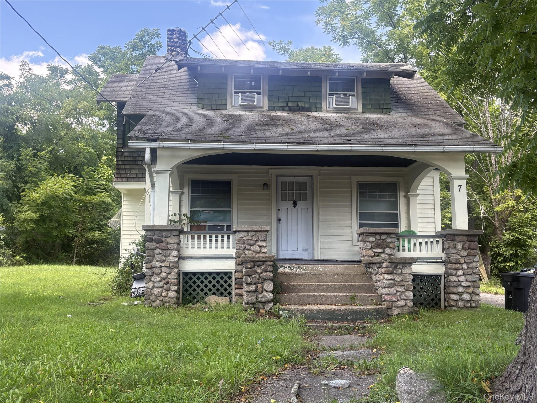 Exterior featuring a covered front porch with stone pillars, wood siding, and a gabled roofline