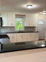 White shaker-style cabinetry with dark countertops, a tile backsplash, and stainless steel hardware