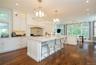 Spacious kitchen featuring white cabinetry, a large center island with seating, dark wood-finish flooring, and multiple windows