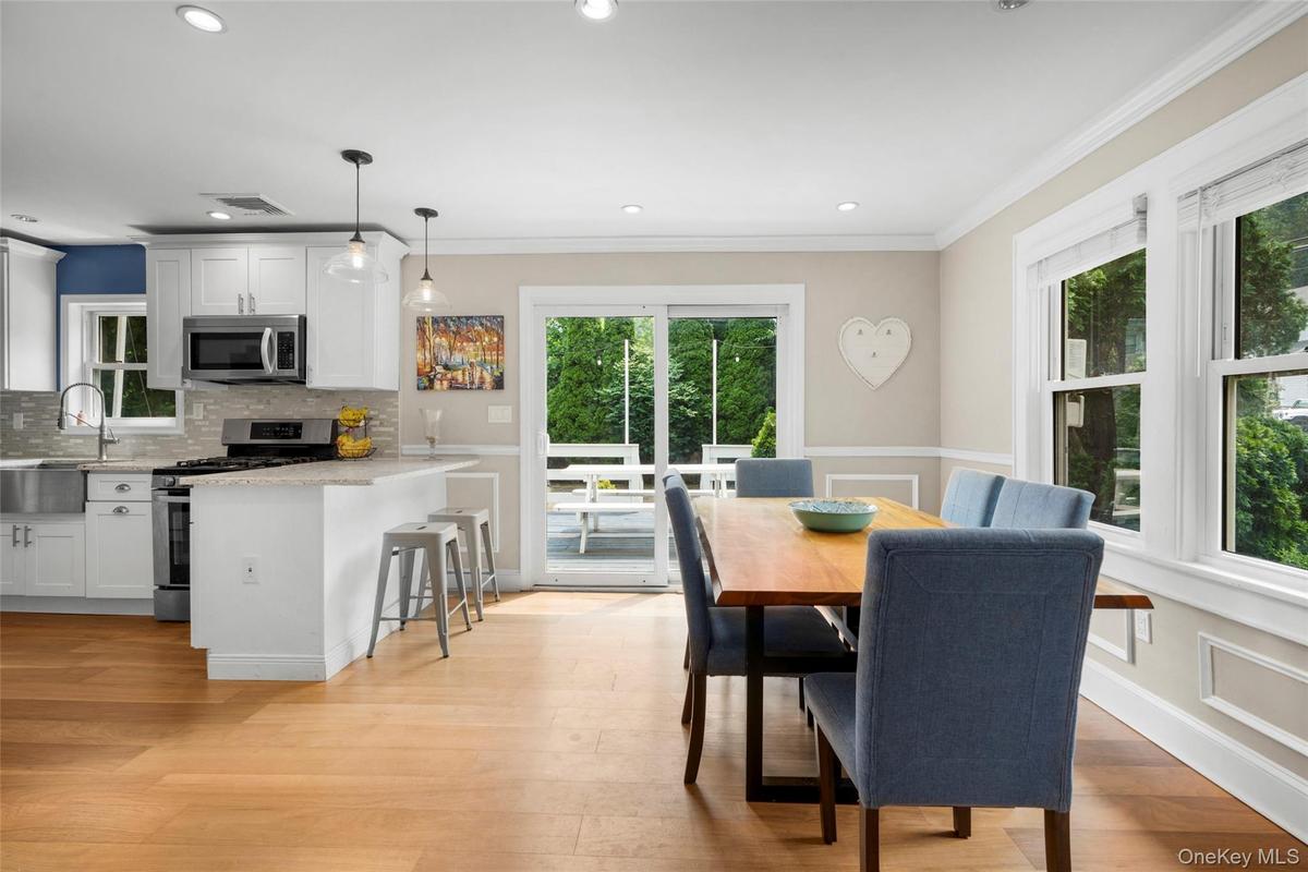 Open-concept kitchen and dining area featuring light wood-finish flooring, white cabinetry, stainless steel appliances, and sliding glass doors to out