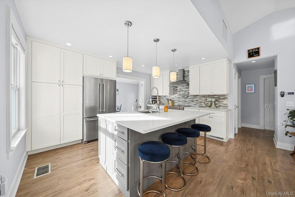 Kitchen with hanging light fixtures, white cabinetry, high quality fridge, a breakfast bar, and a center island with sink