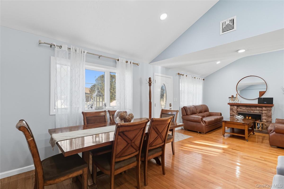 Dining area featuring light wood-type flooring, healthy amount of natural light, a stone fireplace, recessed lighting, and high vaulted ceiling
