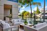 Ground-level waterfront terrace with glass railing, woven outdoor sectional and lounge seating, direct canal views, private dock with yacht, tropical