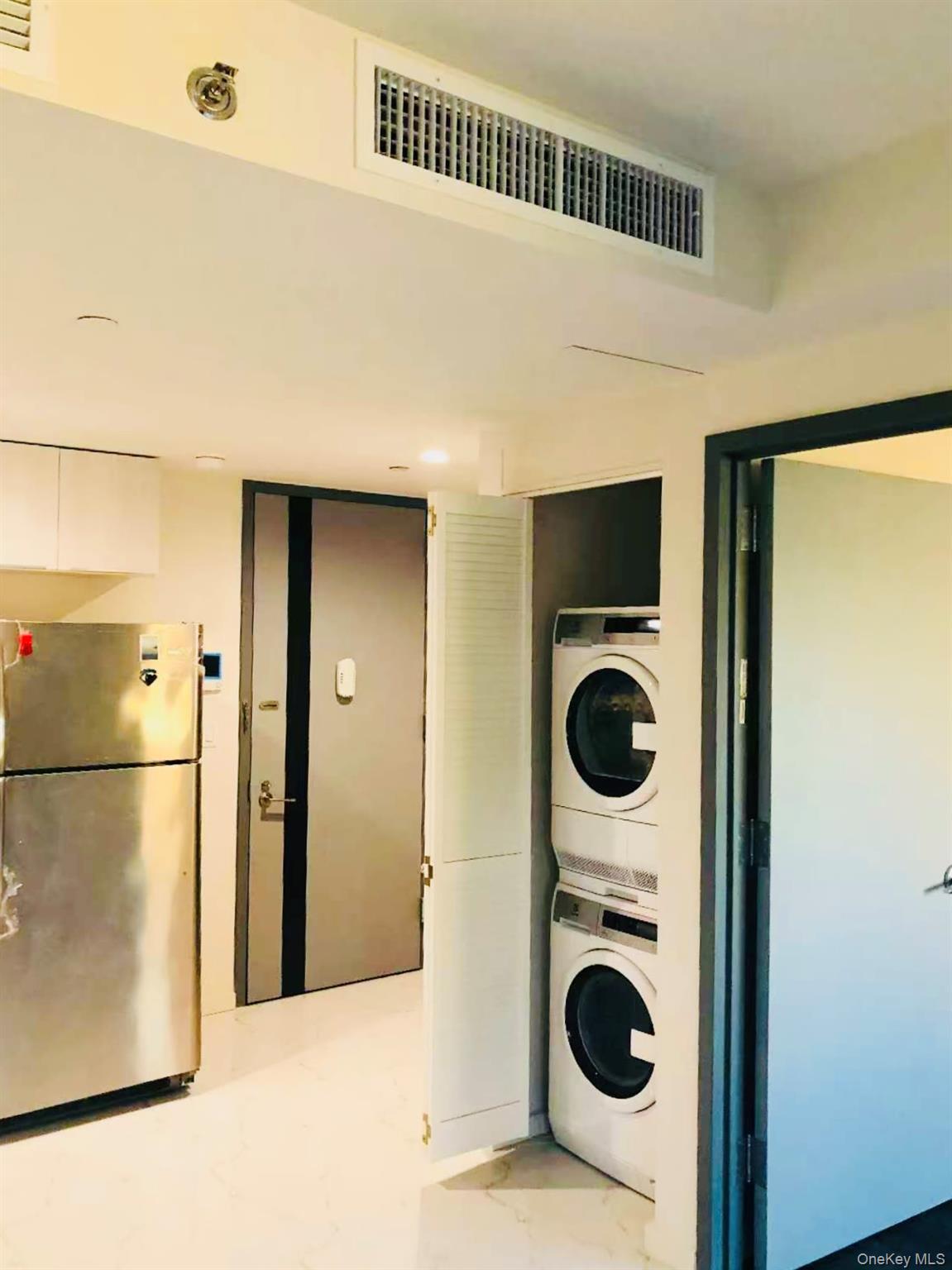 Laundry room with stacked washer / drying machine and light marble finish floors