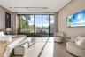 Bright en-suite bedroom with wide-plank light stone floors, upholstered platform bed, tufted bench, curved lounge chairs, wall-mounted TV, track light