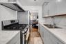 Galley kitchen featuring light gray cabinetry, light marble-patterned countertops, stainless steel appliances, and wood-finish flooring