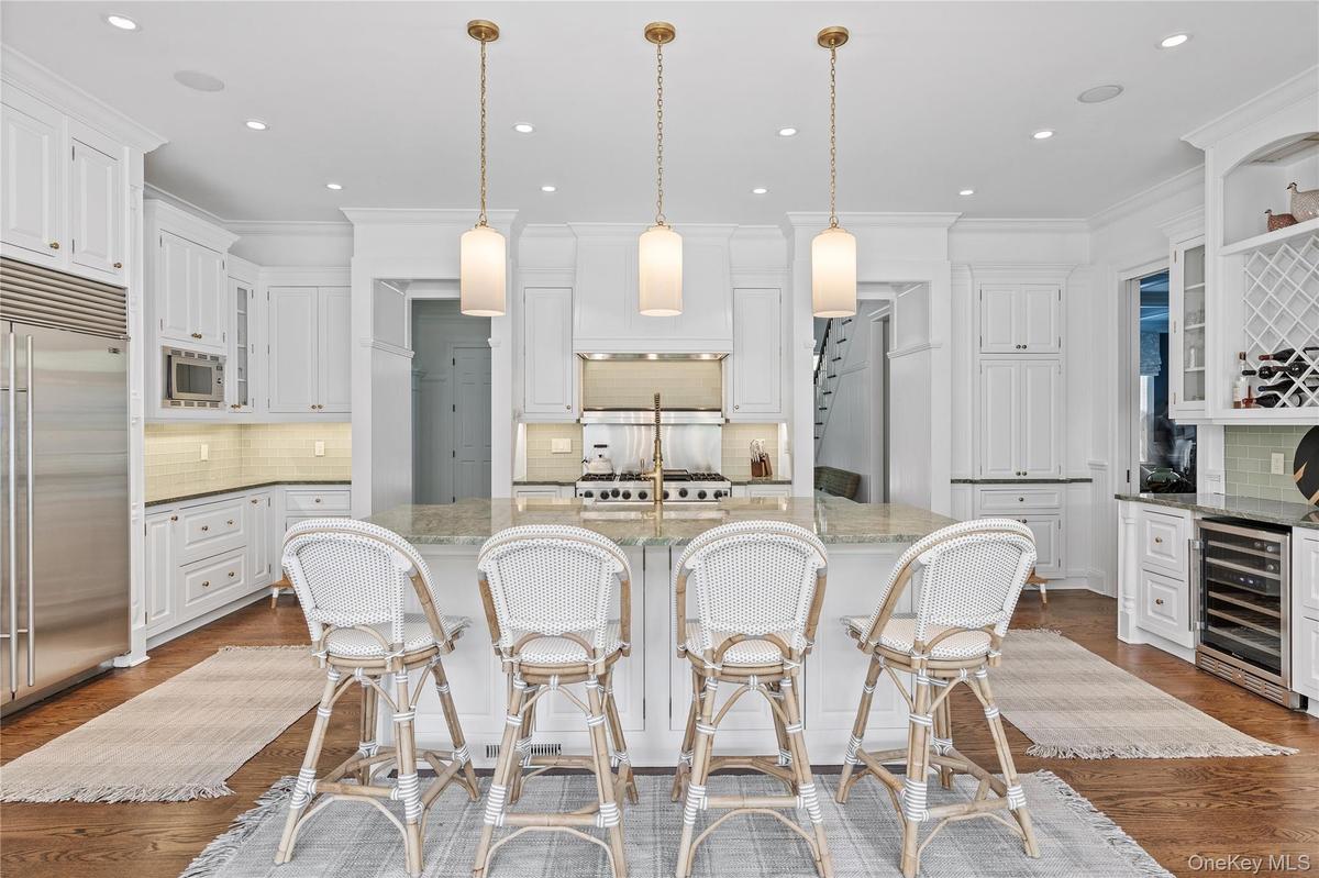 Kitchen featuring decorative backsplash, beverage cooler, glass insert cabinets, built in appliances, and a center island with sink
