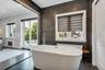 Architectural Digest! Freestanding soaking tub with floor-mounted faucet, dark large-format tile accent wall, dark wood-finish flooring, and a glass-p