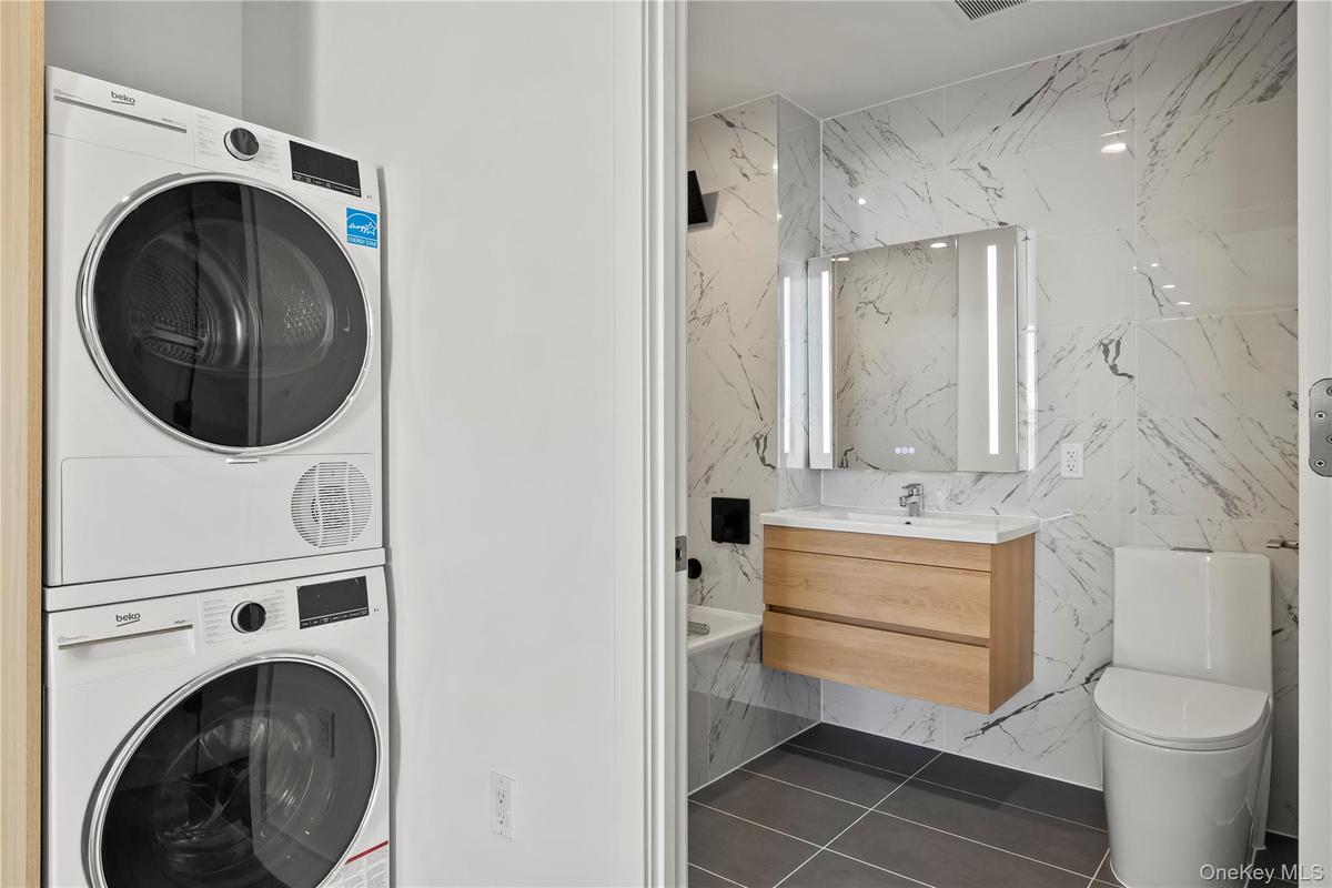 Laundry room featuring tile walls, estacked washer and dryer, and dark tile patterned floors