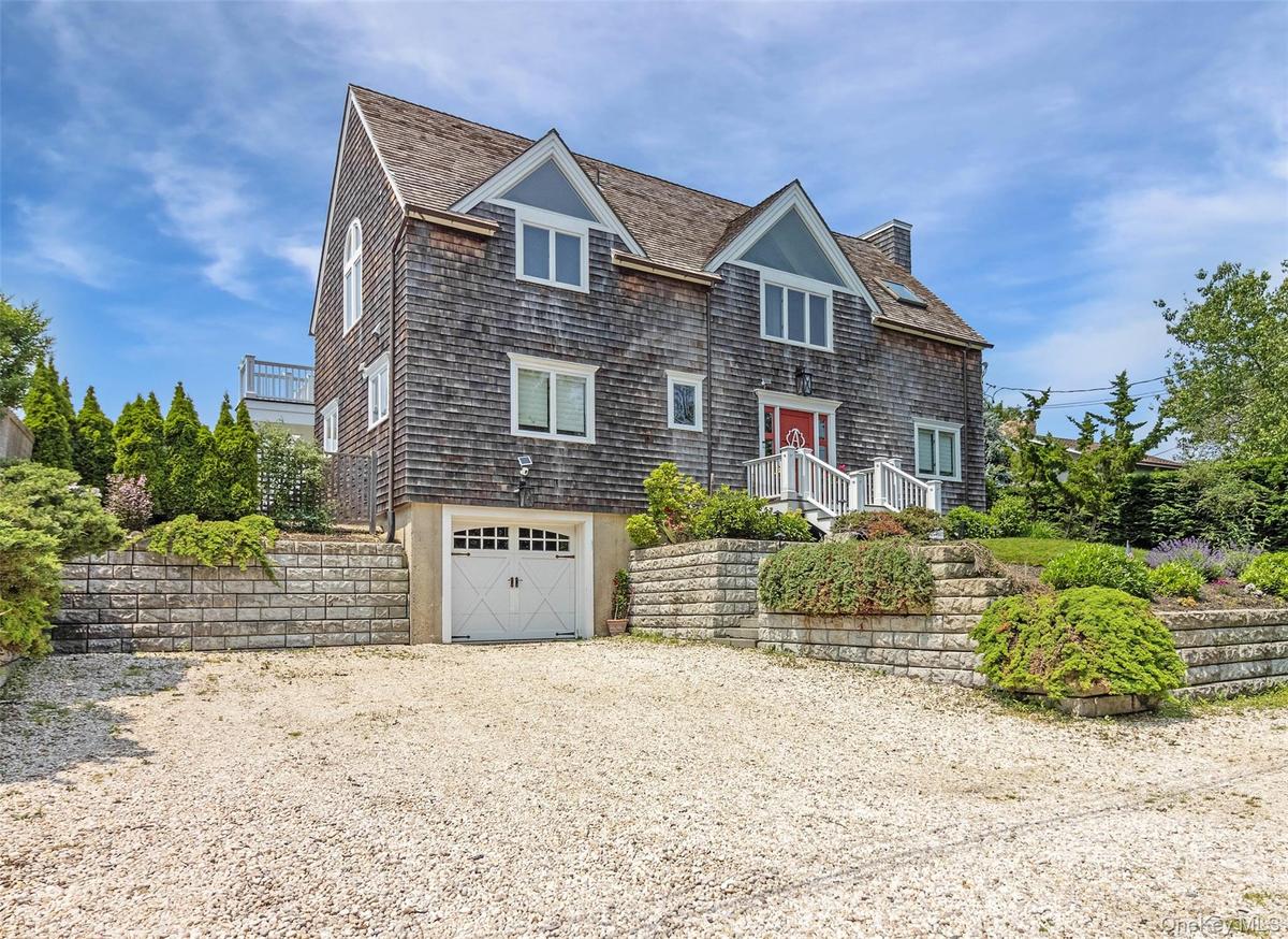 Shingle-style home with driveway, an attached garage, and a chimney