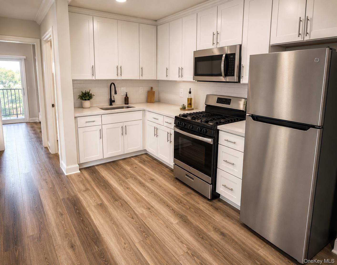 Modern kitchen featuring white shaker cabinetry, stainless steel appliances, light-toned countertops, a subway tile backsplash, and wood-finish floori