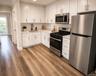 Modern kitchen featuring white shaker cabinetry, stainless steel appliances, light-toned countertops, a subway tile backsplash, and wood-finish floori