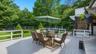 Expansive light-gray decking with white railings, featuring a glass-top dining table with wicker chairs