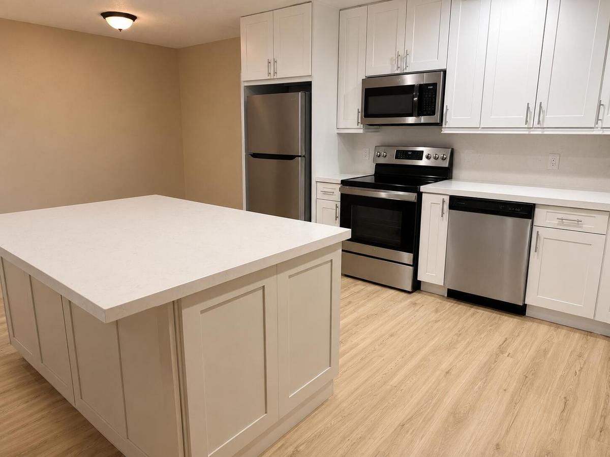 Kitchen featuring a large central island with a light-toned countertop, white shaker-style cabinetry with brushed nickel hardware, and stainless steel