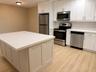 Kitchen featuring a large central island with a light-toned countertop, white shaker-style cabinetry with brushed nickel hardware, and stainless steel