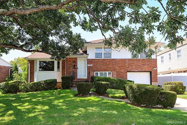 Brick and siding exterior with a garage door, front entry, bay window, and manicured landscaping