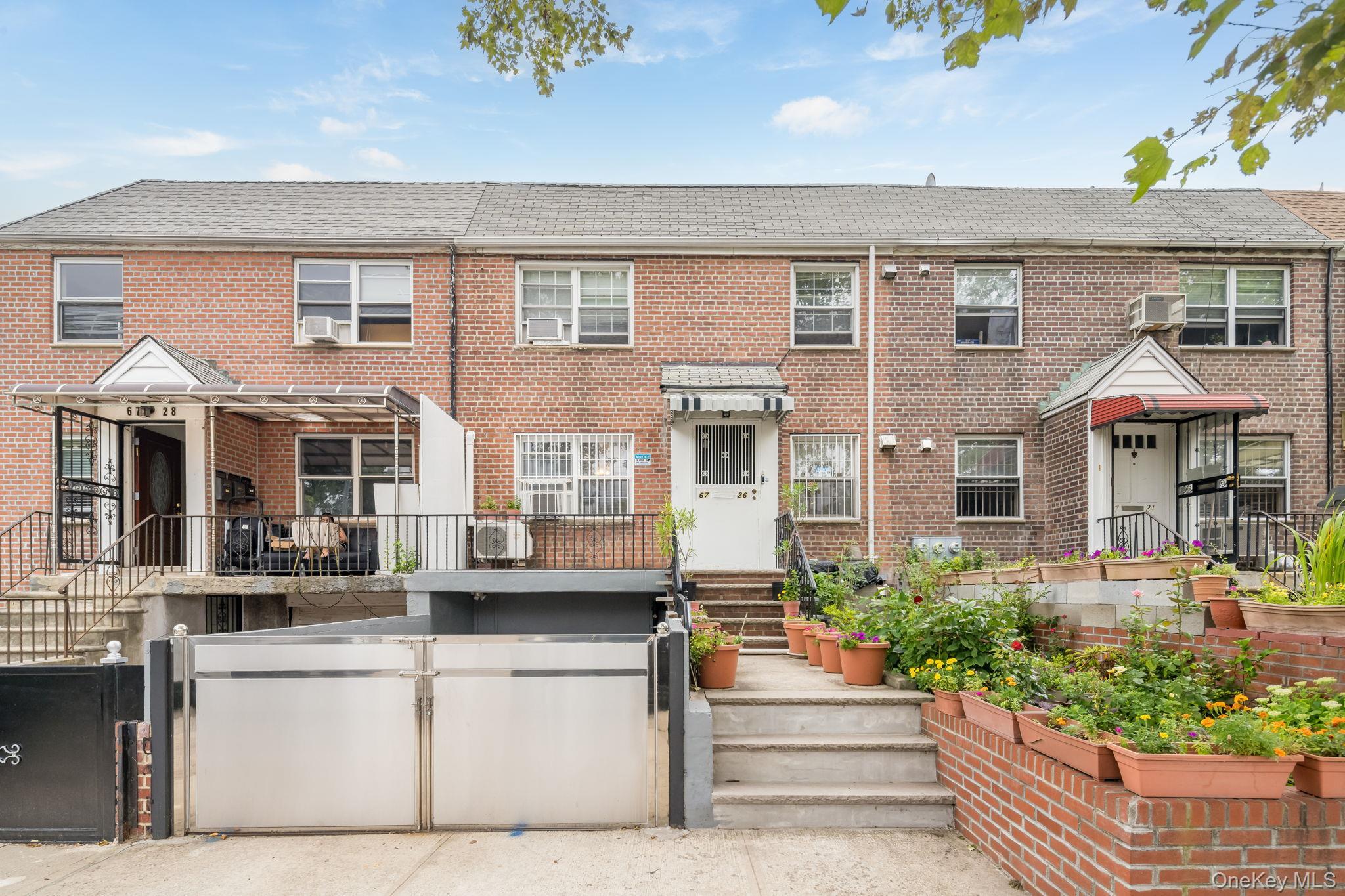 Brick facade with multiple windows, tiered front garden beds, and a paved walkway leading to the entrance