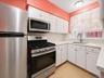 White cabinetry with stainless steel hardware, stainless steel appliances, white subway tile backsplash, light-toned countertops, and wood-finish floo
