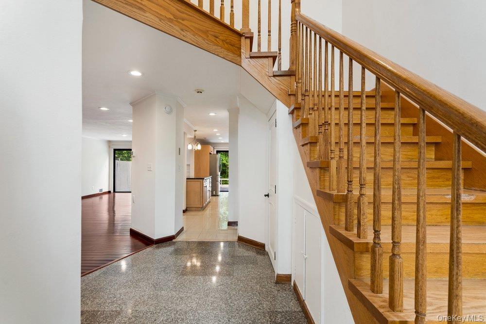 Entry foyer featuring speckled flooring, a natural wood staircase with balusters, recessed lighting, and a doorway opening to a room with dark wood-fi