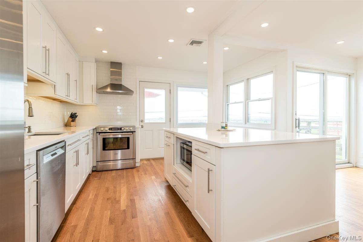 Modern kitchen featuring white cabinetry, stainless steel appliances, solid surface countertops, a center island with built-in microwave, and wood-fin