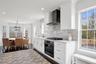Kitchen with wall chimney range hood, stainless steel gas cooktop, black oven, decorative backsplash, and dark wood-style floors