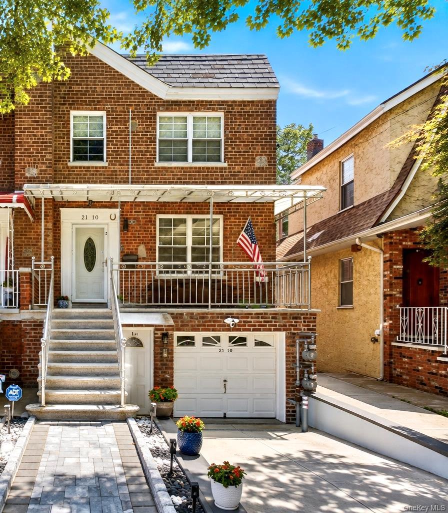 Brick exterior with a gabled roofline, front porch with metal railings, attached garage, paved driveway, and stone paver walkway