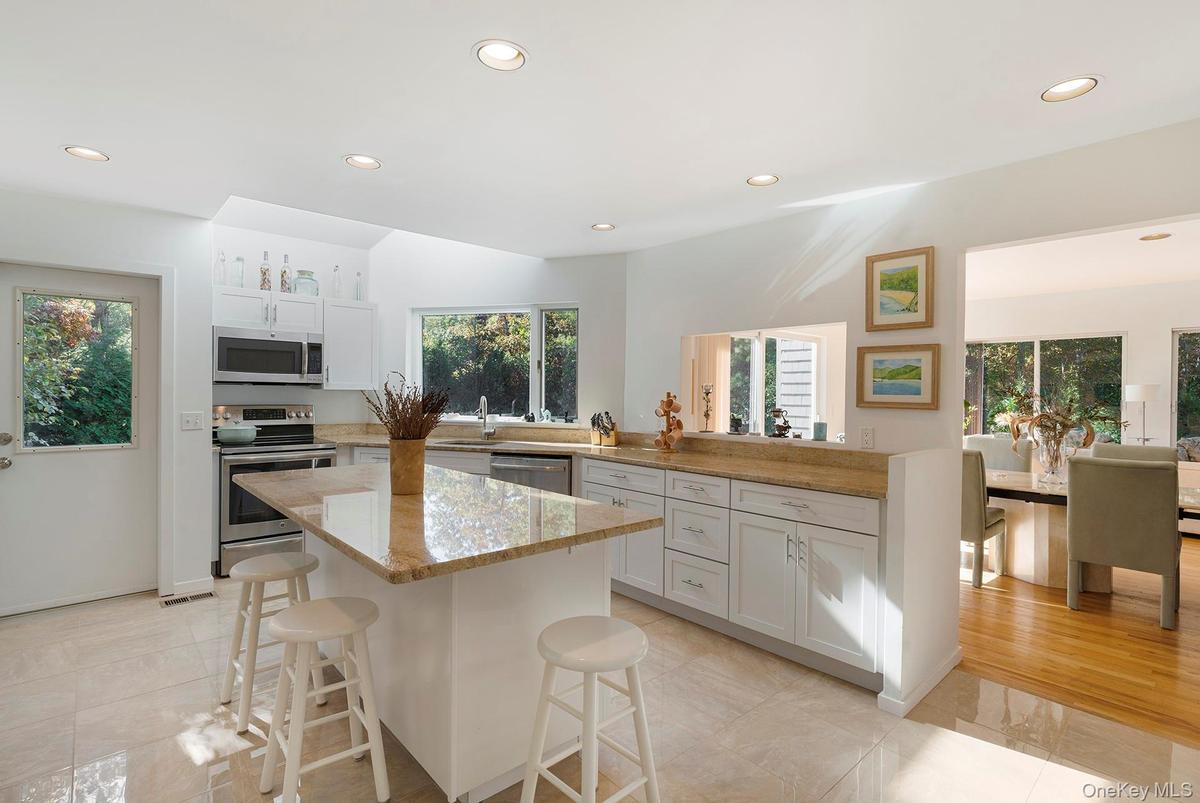 Kitchen featuring recessed lighting, stainless steel appliances, a breakfast bar, white cabinetry, and light stone counters