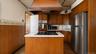 Kitchen featuring wood cabinetry, stainless steel refrigerator, white countertops, built-in oven, and a center island with cooktop