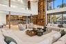 Wide-angle view of open-plan great room and chef's kitchen featuring curved fluted island with stone top, full-height illuminated walnut shelving, dou