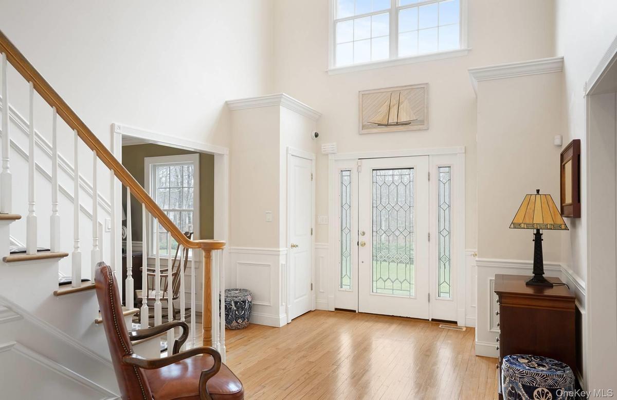 Entryway featuring plenty of natural light, light wood-style flooring, wainscoting, a decorative wall, and stairs