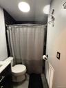 Bathroom featuring a shower with dark subway tile surround, white toilet, and dark vanity with a light-colored countertop.Apt. #1