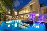 Night view of full rear elevation with illuminated pool, dark mosaic spa, stone-clad two-story facade, floor-to-ceiling glass, circular porthole windo