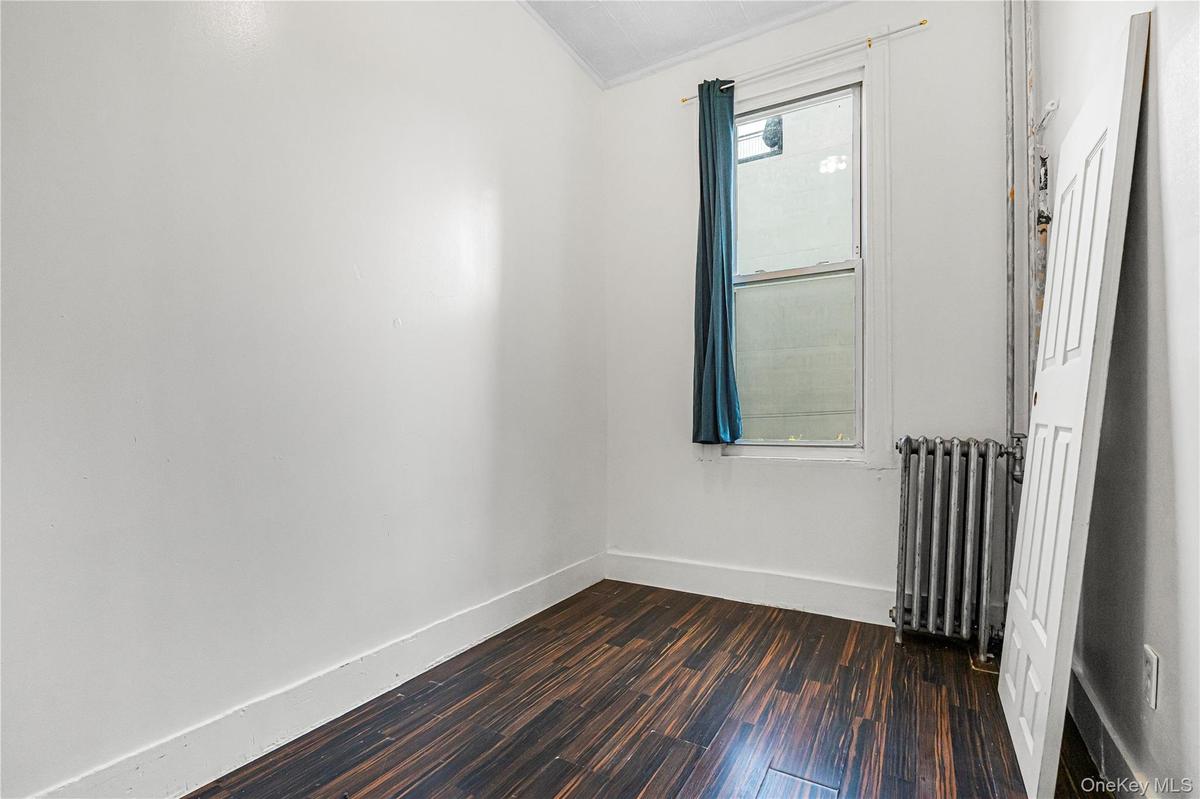 Bright room featuring wood-finish flooring, white walls, and a window with a dark curtain