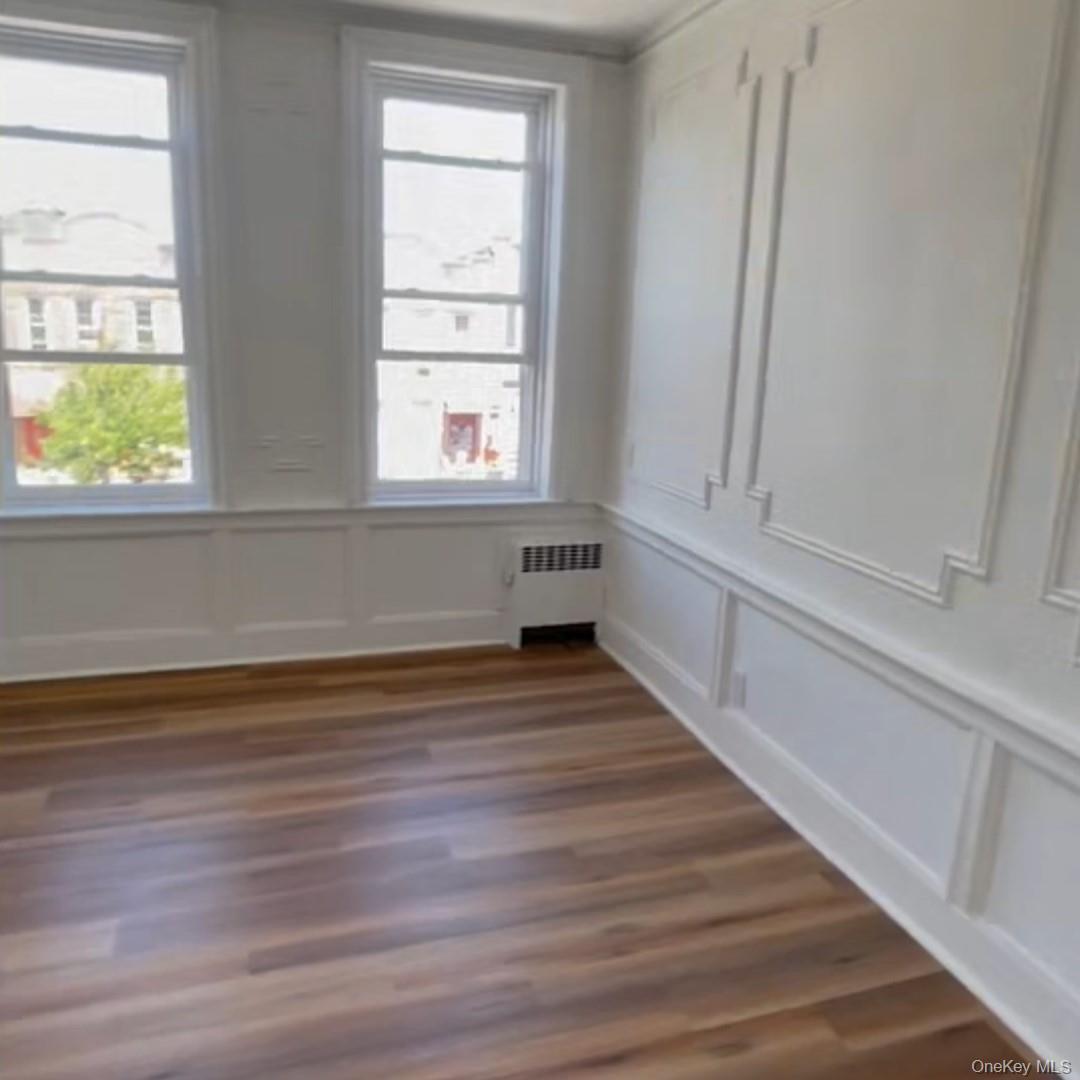 Empty room with a decorative wall, radiator, and dark wood finished floors