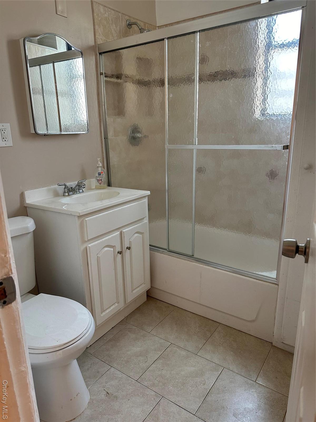 Full bath featuring combined bath / shower with glass door, light tile patterned flooring, and vanity