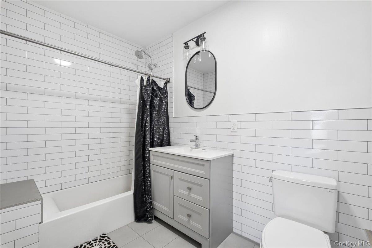 1st Floor Apartment Bathroom featuring white subway tile walls, a bathtub with a shower, a vanity with a sink, and a toilet