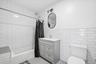 1st Floor Apartment Bathroom featuring white subway tile walls, a bathtub with a shower, a vanity with a sink, and a toilet