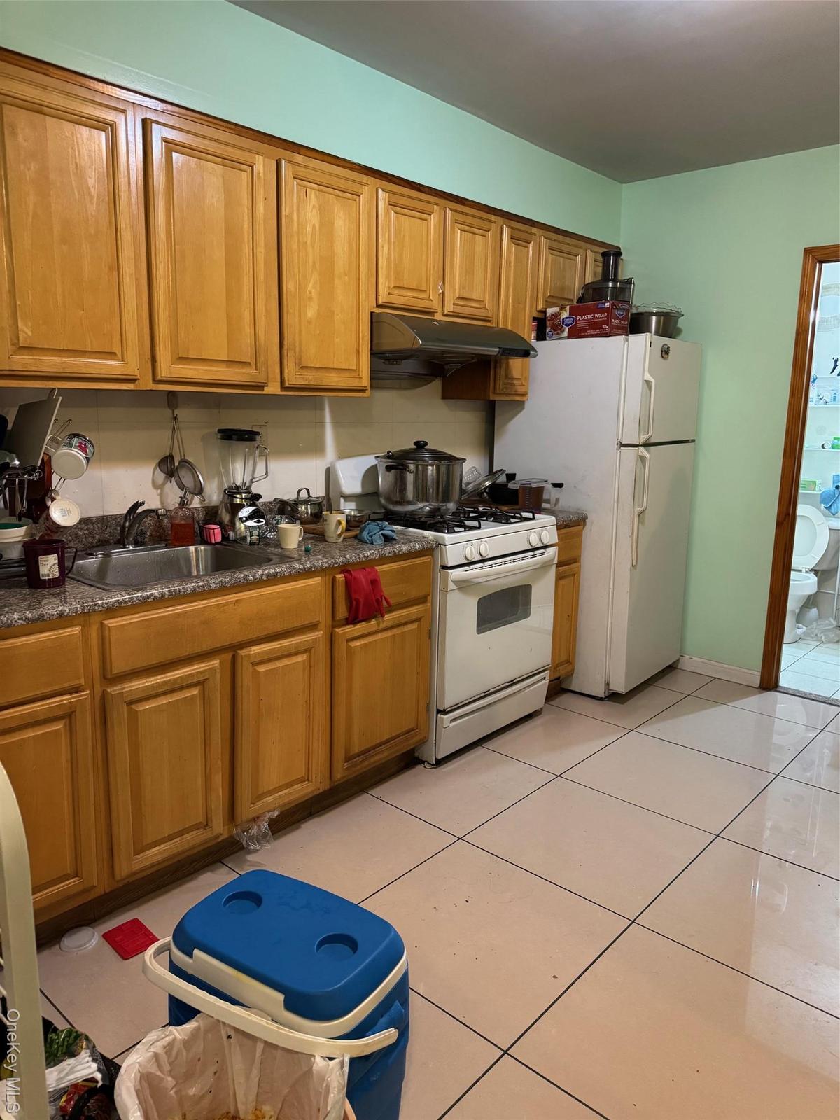 Kitchen featuring white gas stove, brown cabinetry, range hood, and light tile patterned floors